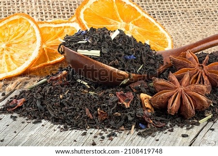 Black blended tea with flower petals and dried fruit in wooden spoon on a wooden desk. Black tea, anise stars and dried oranges.