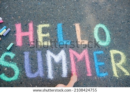 Sidewalk chalk games for kids concept. Top view of girl drawing multicolored inscription Hello summer on pavement on sunny day. Selective focus