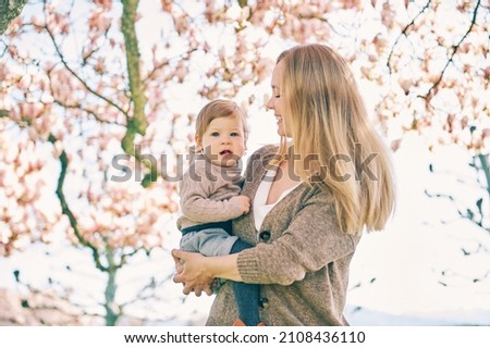 Outdoor portrait of happy young mother with adorable baby girl under blooming spring tree, bottom view