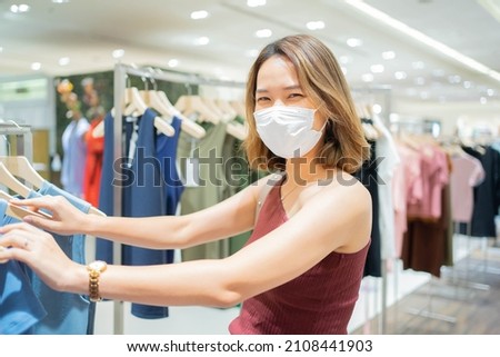 close up young woman wear face-mask and choosing dress at fashion zone shop in department store for new normal lifestyle and shopaholic concept