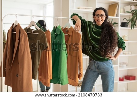 Happy Female Designer Standing Near Clothing Rail Smiling To Camera Presenting New Collection Posing In Modern Showroom, Smiling To Camera. Fashion And Style, Design Career Concept Royalty-Free Stock Photo #2108470733