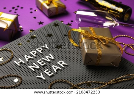Board with text HAPPY NEW YEAR, gift boxes and Christmas decor on color background, closeup