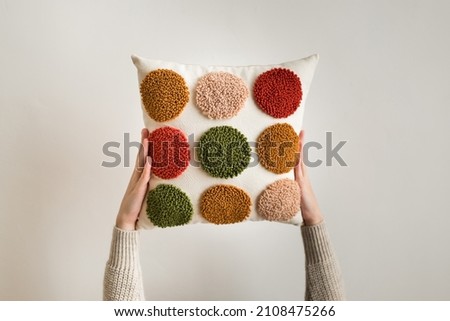 Punch needle embroidery pillow diy. Close up of woman hands holding pillow. Product is made according to the technique pushing woolen threads on foundation fabric with needle with wood handle  Royalty-Free Stock Photo #2108475266