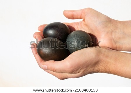 photo of eggs painted black, in women's hands on a white background. Easter theme