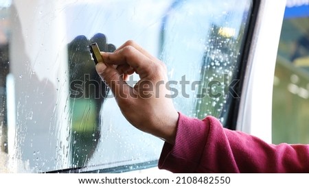 Handle the blade to clean the windshield. A mechanic uses a razor blade to scrape off the glue from the glass to clean it before installing the new film. selective focus Royalty-Free Stock Photo #2108482550