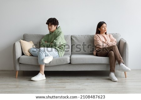 Annoyed young Asian couple sitting on couch in silence after fight, looking in opposite directions at home. Offended spouses ignoring each other. Family conflict, separation, divorce, breakup Royalty-Free Stock Photo #2108487623