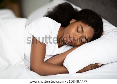 Closeup shot of peaceful young curly african american woman sleeping in comfortable bed alone at home, enjoying her high quality orthopedic mattress. Bedroom furniture, bedding concept Royalty-Free Stock Photo #2108487779
