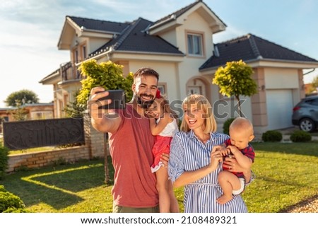 Beautiful happy family having fun taking selfie using smart phone in front of their new house