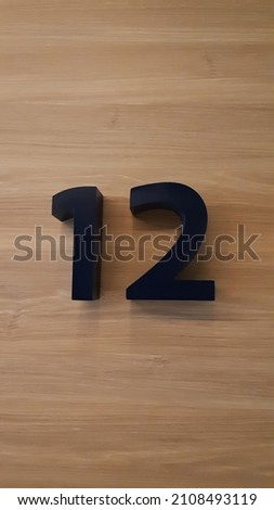 Block number twelve on a brown wooden wall background. Numeric sign or symbol.