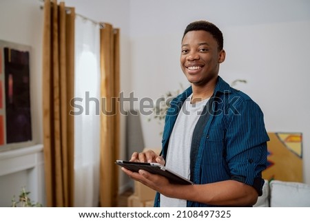 A man stands in middle of an apartment about the renovation, a new house, in the living room there are moving cartons, the boy holds a tablet in hands, looking for flat device inspiration