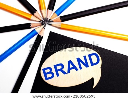 Wooden card with the text BRAND on a black background near multicolored pencils.