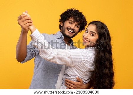 Romantic happy indian husband and wife hugging, holding hands and dancing, having date, yellow background. Happy marriage, romance concept