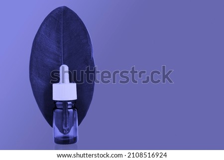 Bottle with pipette of herbal essential oil. Essential oil in glass bottle with fresh green leaf in tinted trendy purple color Very Peri. copy space. High quality photo