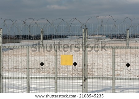 barbed wire fence of a restricted area with a closed gate and yellow warning sign with copy space