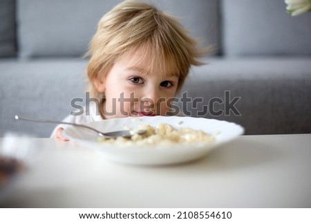 Cute toddler boy, eating pasta with white cheese at home for lunch