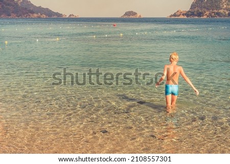a tanned boy swimming in the sea bay with clear blue water