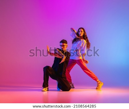 Strange body movements. Two young people, guy and girl dancing contemporary dance over pink background in neon light. Modern dance aesthetics concept Royalty-Free Stock Photo #2108564285