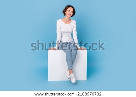 Photo of girlish adorable woman wear white shirt sitting white cube chair isolated blue color background Royalty-Free Stock Photo #2108570732