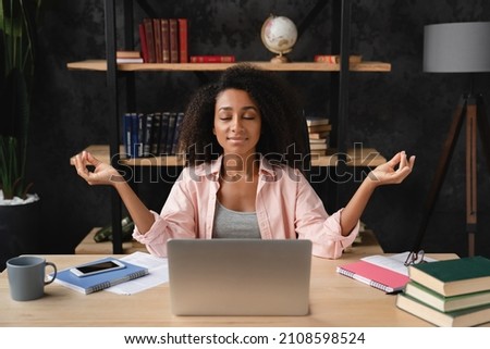 Young african freelancer worker businesswoman student meditating at workplace desk after working hard with homework, e-learning, feeling overworked and stressed Royalty-Free Stock Photo #2108598524