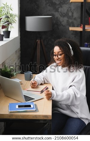Vertical shot of young african woman teenage girl doing homework, assignment on laptop remotely from home, watching webinar, e-learning online. Social distancing concept Royalty-Free Stock Photo #2108600054