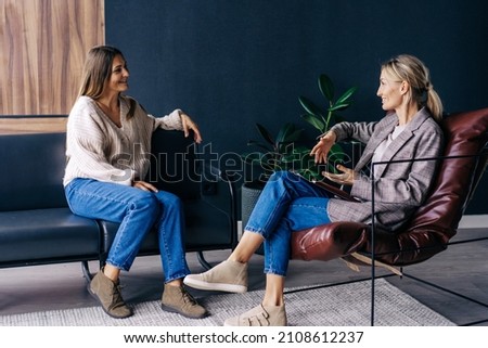 Two modern stylish women are sitting in the office discussing ideas and implementation of plans. A confidential conversation between a woman and a consultant psychologist. Royalty-Free Stock Photo #2108612237