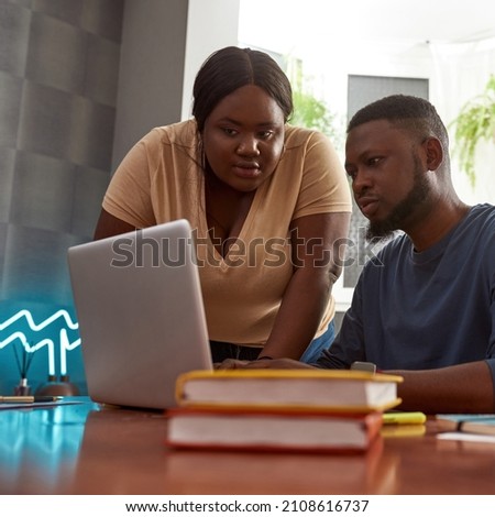Black couple watching something on laptop computer during working at home workplace. Concept of freelance and remote work. Idea of cooperation and teamwork. Young millennial man and woman at desk