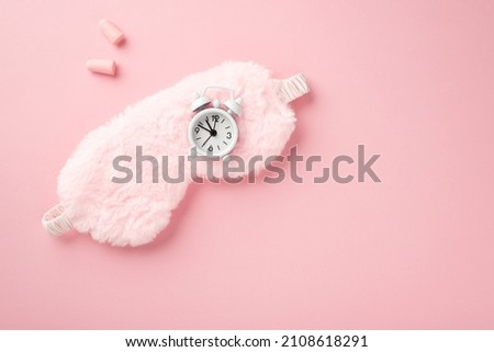 Top view photo of pink fluffy sleeping mask small white alarm clock and earplugs on isolated pastel pink background with copyspace