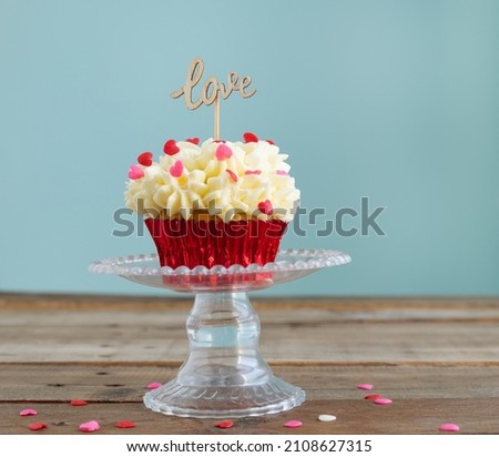 Cupcake on a display stand with cream and red topping decoration on a wooden background with a sign with the word LOVE. Valentine's Day. Copy space.