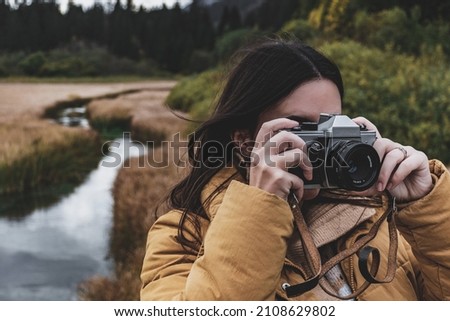 A Portrait of a young woman taking photos of beautiful fall nature with a vintage camera