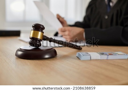 Law, auctioning, corruption, bankruptcy, bail, bribery or fines. Close up of judge gavel standing on sound block and bundle of dollars on table against background of judge or auctioneer with documents Royalty-Free Stock Photo #2108638859