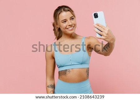 Young strong sporty athletic fitness trainer instructor woman wear blue tracksuit spend time in home gym doing selfie shot on mobile cell phone isolated on plain pink background. Workout sport concept