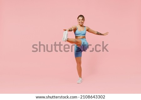 Full body young strong sporty athletic fitness trainer instructor woman wear blue tracksuit spend time in home gym do exercise raise leg isolated on plain light pink background. Workout sport concept.