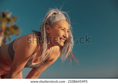 Adult strong female after good workout standing leaning down and looking ahead on warm sunny day by the waterfront Royalty-Free Stock Photo #2108645495