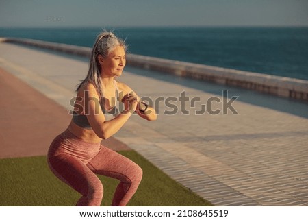 Active sporty woman performing squats on the sports street playground by the coast on warm sunny day Royalty-Free Stock Photo #2108645519
