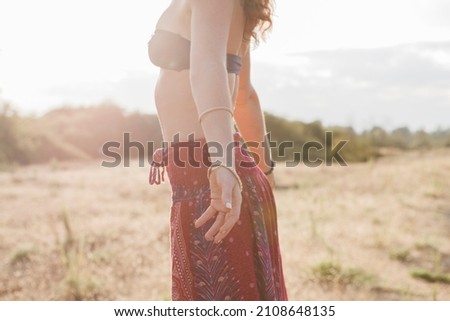 Boho woman in bikini top skirt arms outstretched in sunny rural field