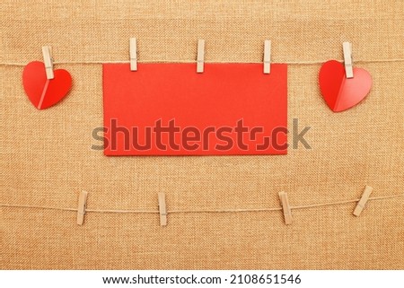 red hearts with paper note for text on clothes pin on brown textile background.