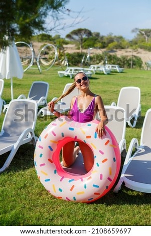 A young woman in a stylish swimsuit and sunglasses holds an inflatable donut ring in her hand. Beautiful happy girl posing and having fun in the sun. Vacation. travel