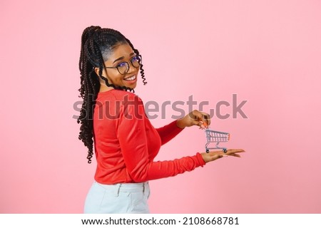 Young african american girl holding small supermarket shopping cart, smiling.