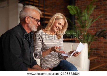 Senior joyful husband and wife look at the mail. Paper work together. A nice bonus for a mature couple. Royalty-Free Stock Photo #2108693684