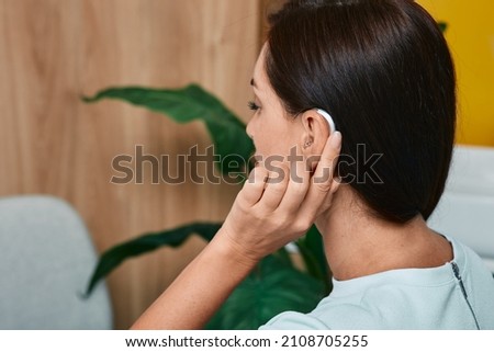 Adult woman tunes her hearing aid behind the ear by pressing her finger on setting button. Modern hearing aid, hearing solutions Royalty-Free Stock Photo #2108705255