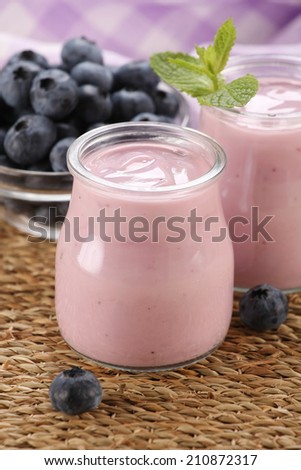 yogurt with blueberries in a glass jar and blueberries in a glass bowl on a background of  wicker mat