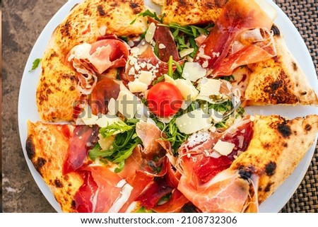 Top view of plate with delicious Italian pizza with prosciutto, arugula, fresh tomatoes and shaved parmesan cheese.