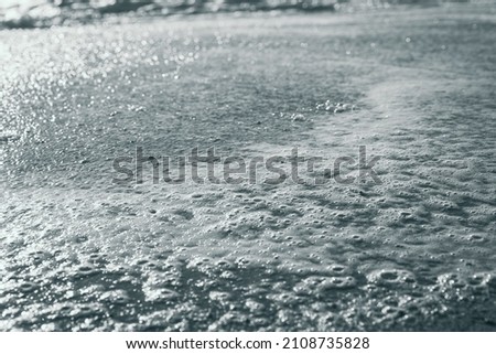 Close up on foam at sea shoreline with sun reflection on water. Abstract background concept. Black and white photography