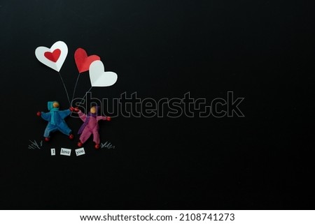 2 gender neutral characters holding heart balloons on a chalkboard background, horizontal orientation, black background, copy space