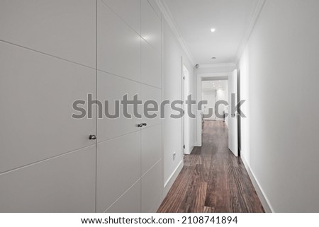 Long hallway with wall covered in white fitted wardrobes with dark wooden floorboards