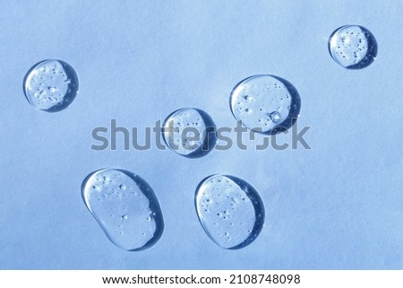 Cosmetic hydrating product or ingredient concept. Blue drops of transparent liquid on a light background. Drops gel or oil close up. Abstract backdrop. Royalty-Free Stock Photo #2108748098