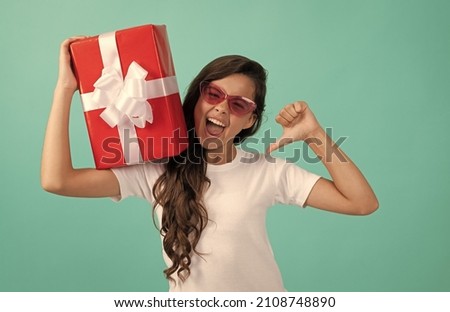 fashionable happy child in sunglasses hold gift box point finger, sale