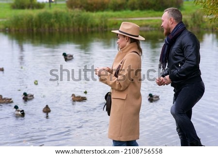 Happy romantic couple in love, beautiful young woman and handsome man is dating, walking together outdoors in park and feeding birds, ducks in a lake or pond. Happiness Royalty-Free Stock Photo #2108756558