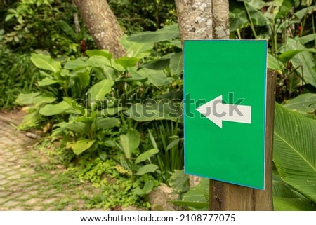 close-up of a green sign with white arrow pointing to tropical vegetation in the background