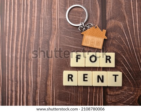 Top view house keychain with text FOR RENT on wooden background.